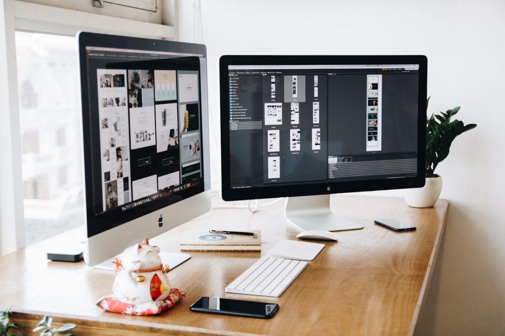 two-imac-s-with-keyboard-and-phones-on-desk-326503 A well-organized design workspace with dual monitors and design software on display.